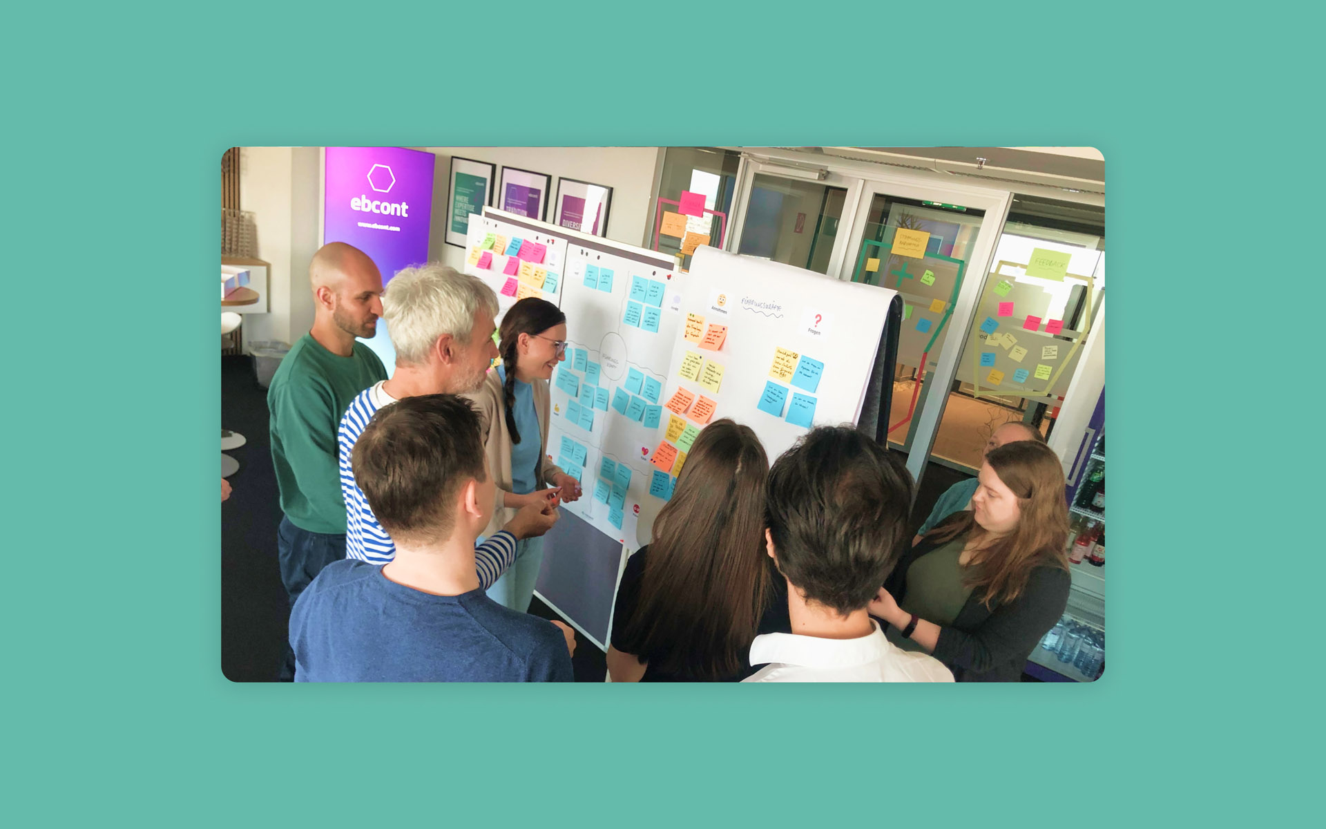 Emanuel-Jochum-Case-Study-EBCONT-Training-Hero-Full-Colour-BG Case study hero image about EBCONT showing people in good mood0 in front of a flipchart adding sticky notes and discussing